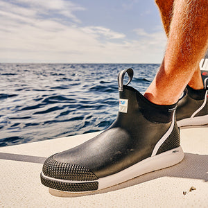 A close up photo of a man wearing a pair of black Xtratuf ADB Sport Boots on a motorised boat at sea