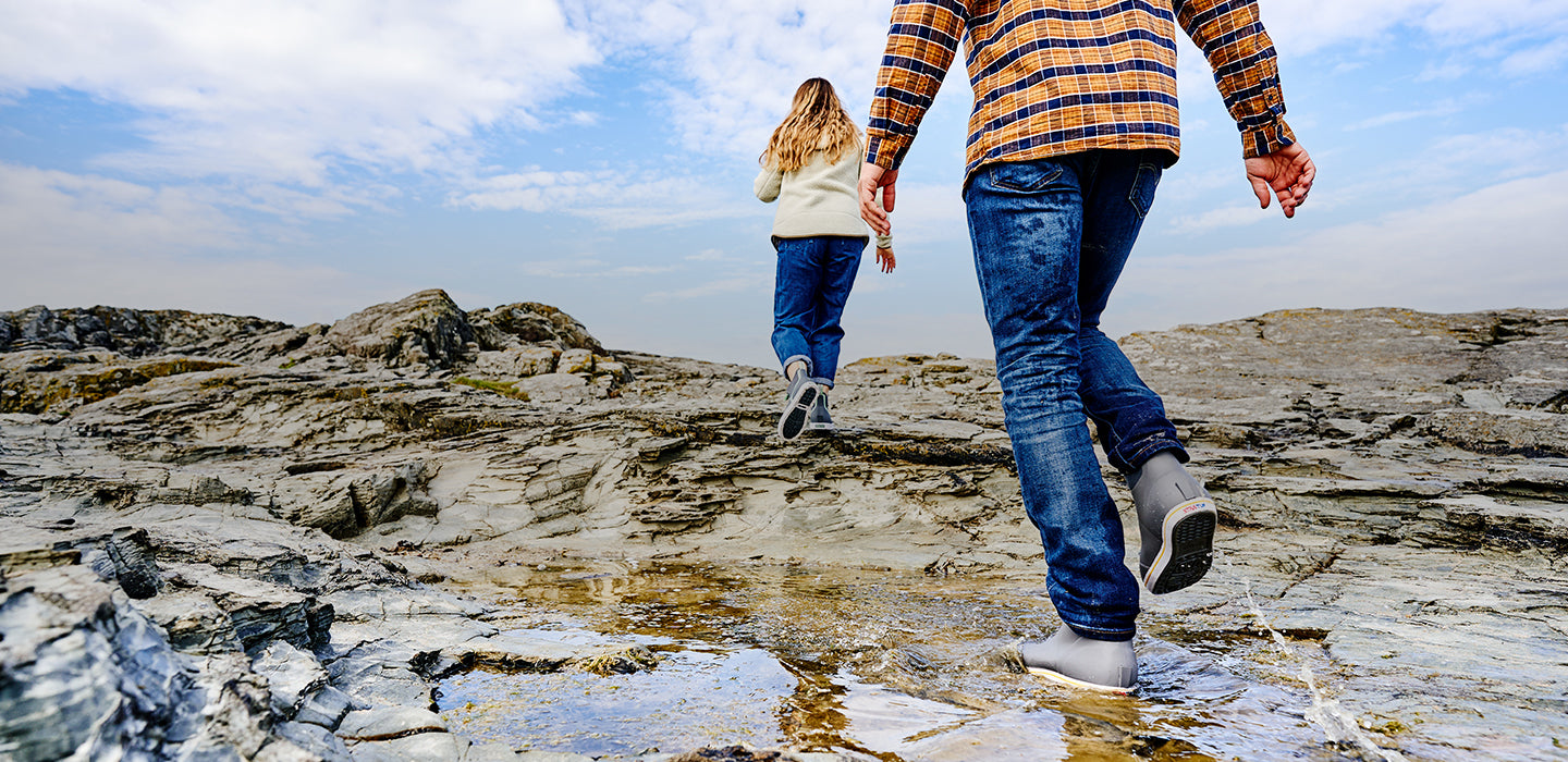 People walking along a rocky shore wearing Xtratuf boots