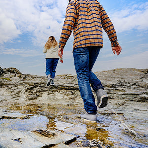 People walking along a rocky shore wearing Xtratuf boots